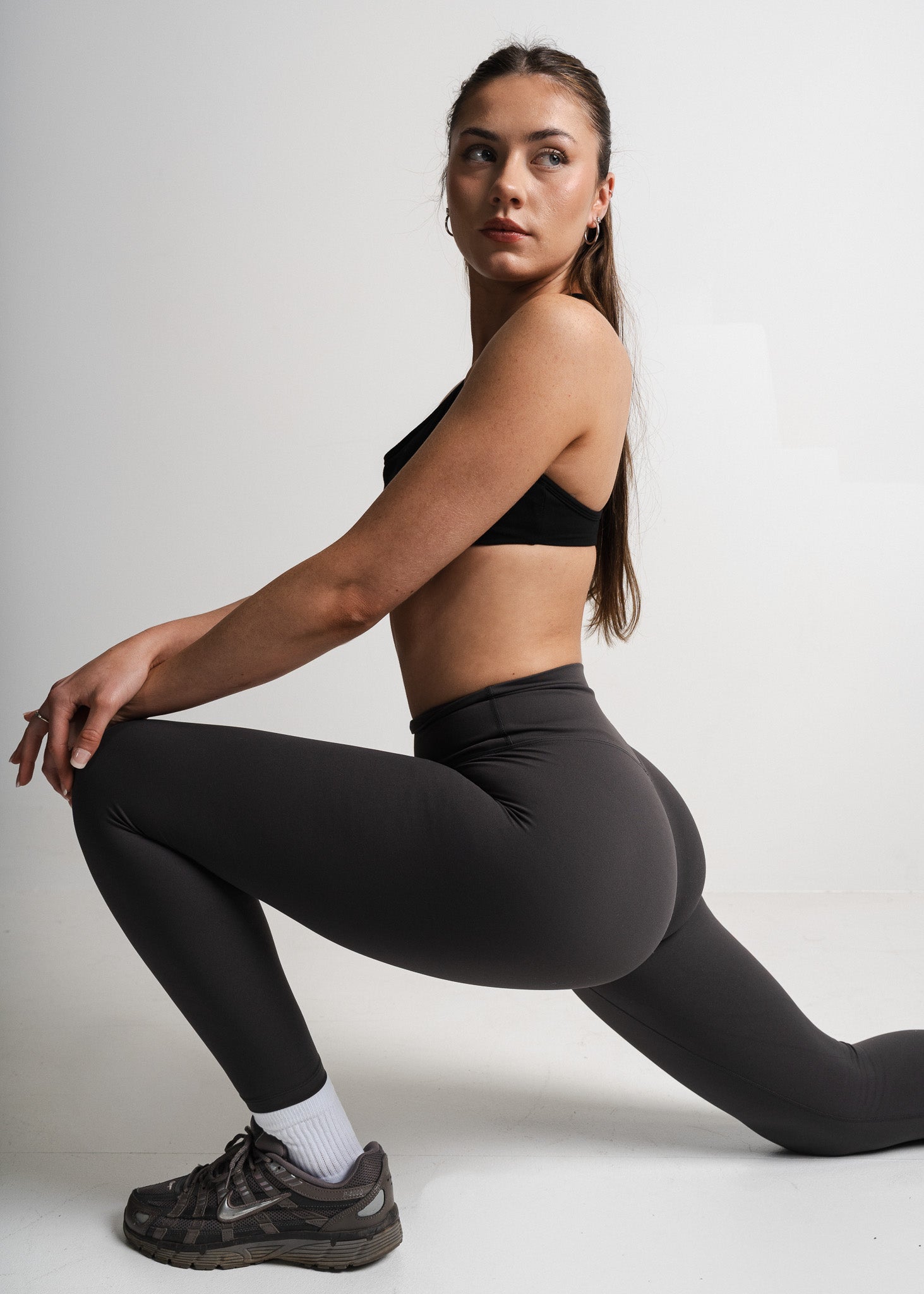 Woman wearing black athletic leggings and sports bra posing against a white background